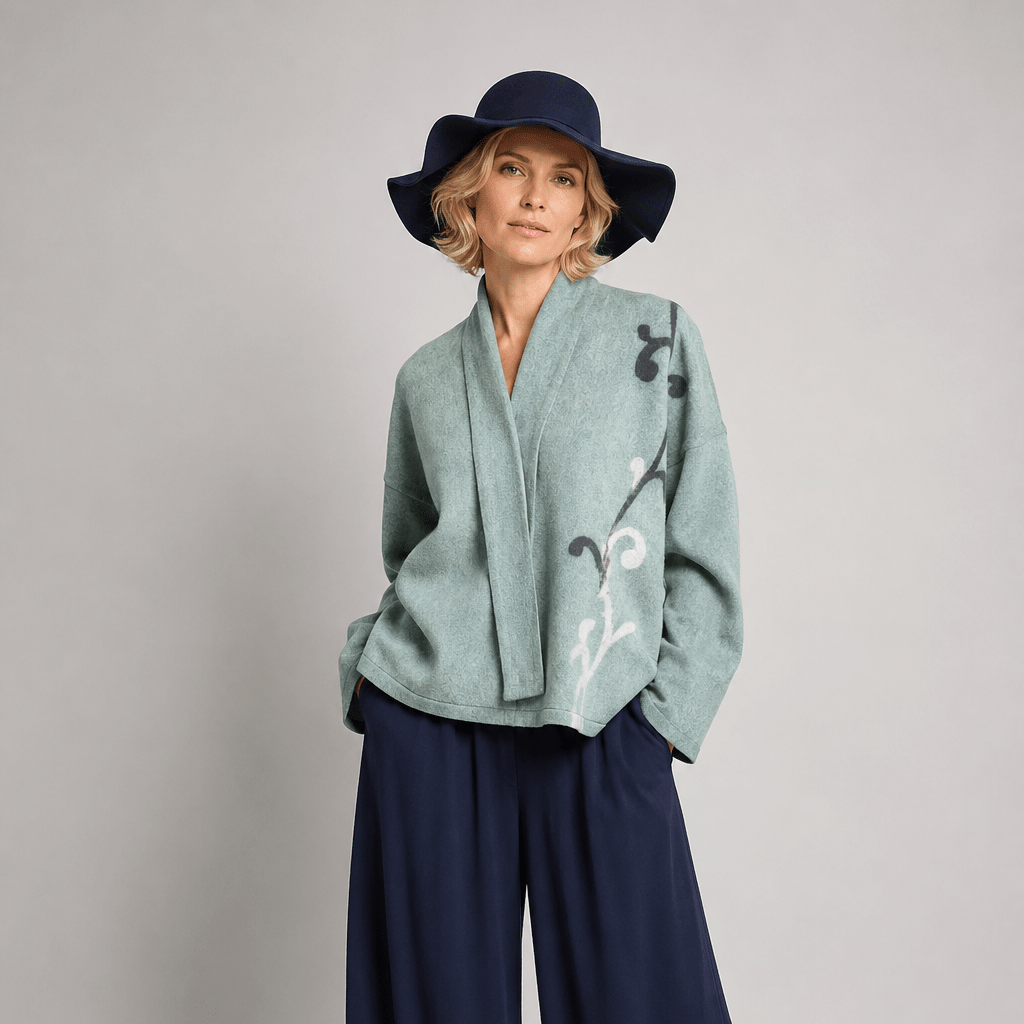 Nuno Milano Lightweight Sage Green Arabesque Kimono Jacket, front view, with hand-felted charcoal and white Arabesque motif, open front, styled with navy wide-leg trousers and navy floppy hat