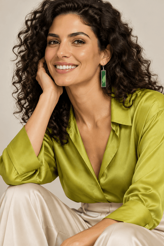 A model wearing a pair of chartreuse and dark green slim, long, rectangular earrings. She's wearing a silk chartreuse blouse and cream silk pants.