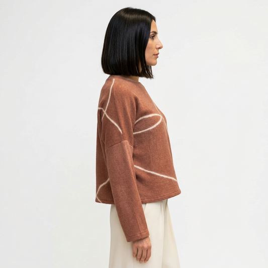 A woman shown from the side wearing a dusty rose cropped sweatshirt with white abstract curved line patterns, paired with cream tailored pants.