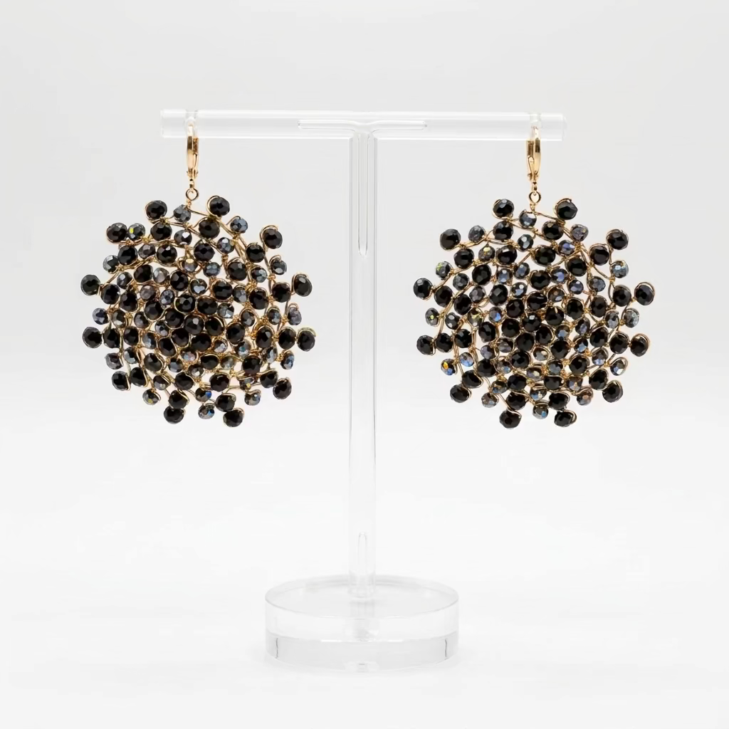 A pair of large black mandala earrings made from onyx zirconias and gold wiring, hanging from a stand against a white background.