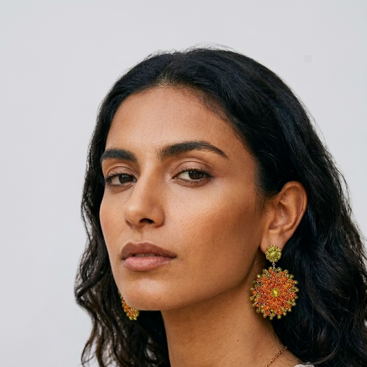 A woman with long dark wavy hair wearing a pair of round orange and lime crystal mandala earrings.