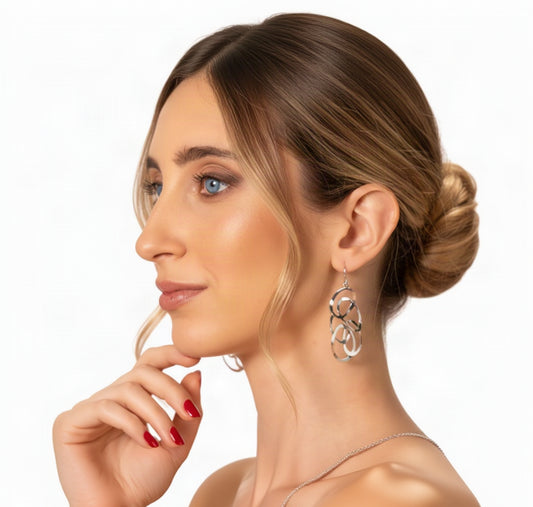 A close-up side profile of a woman wearing a dangling hoop earring with layered, open circular metalwork in a silver-tone finish.