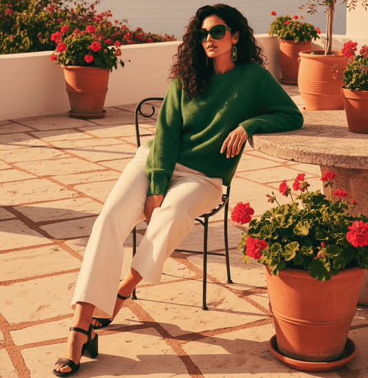 A woman with large sunglasses sitting on a sun drenched patio wearing a pair of long rectangular pendant earrings with dark green and lime inlays.