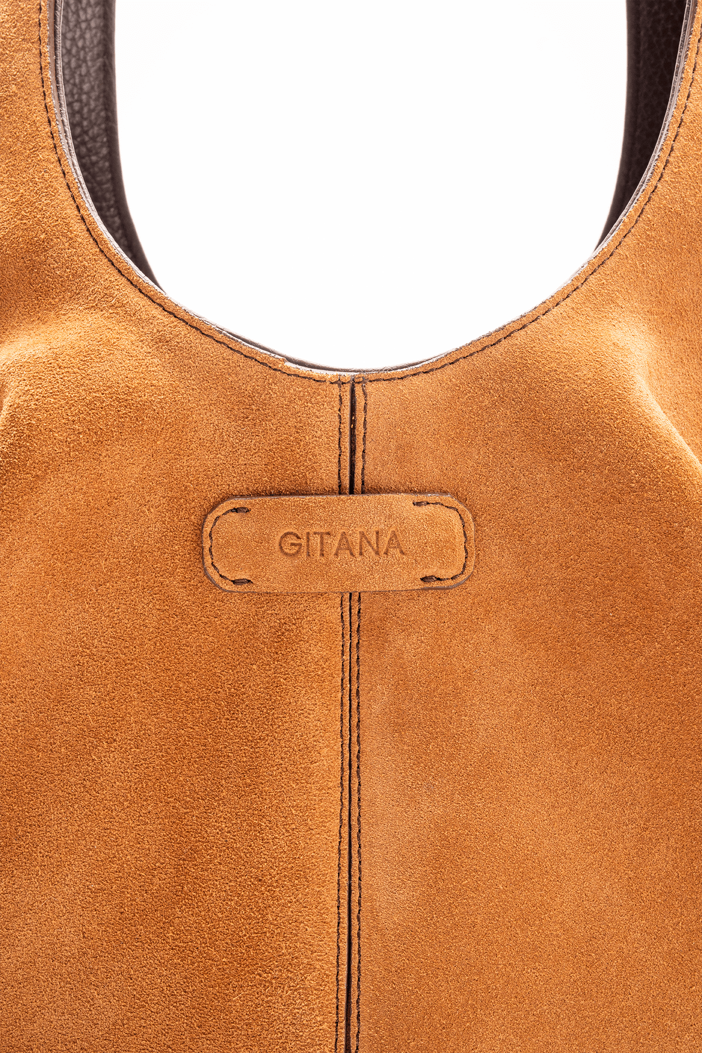 Close-up detail of the Gitana suede tote bag in warm tan leather, featuring the embossed Gitana logo patch, curved top handle, contrast stitching, and soft textured suede finish.