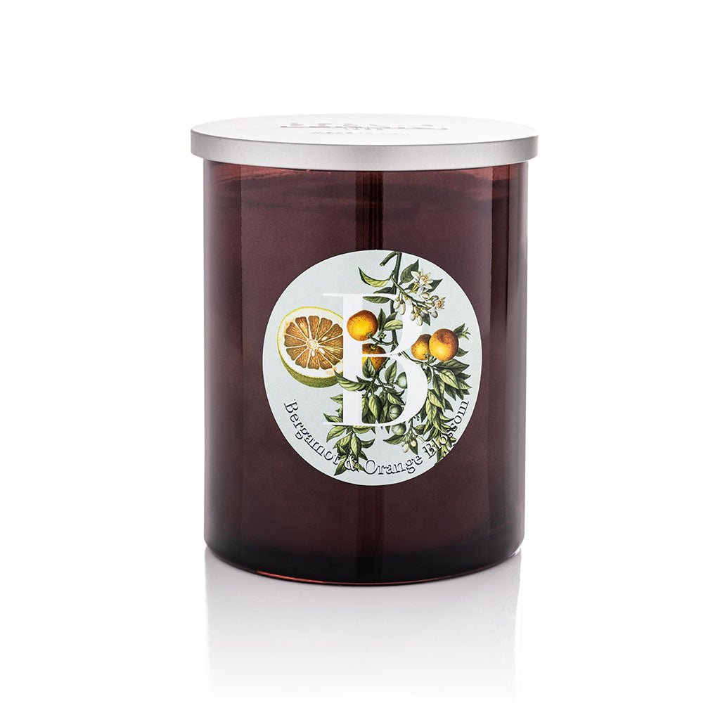 Bergamot & Orange Blossom scented candle in a dark amber glass jar with silver lid, featuring a botanical illustrated label with citrus fruits and orange blossom, product shot on white background