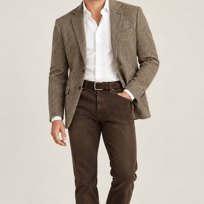 A man wearing a tweed blazer, a white shirt, brown jeans and  dark brown suede belt with a silver buckle.