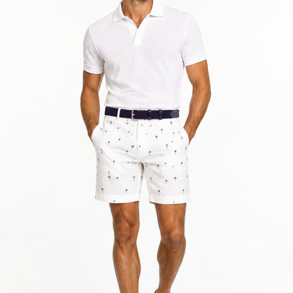 A man wearing a white polo shirt, white linen shots with a navy pattern and a navy woven belt on a white background.