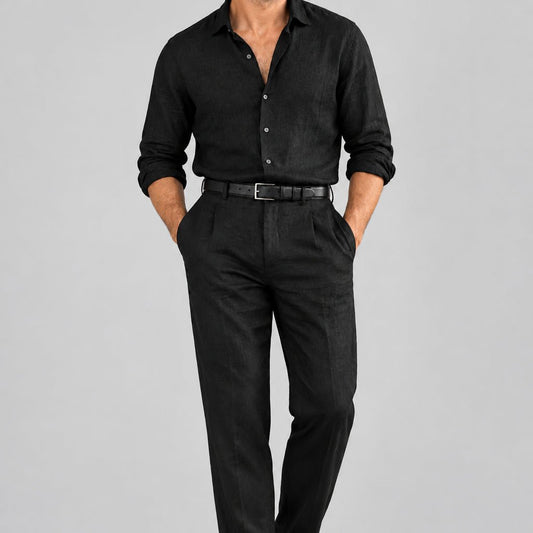 Un homme en chemise et pantalon de lin noirs avec une ceinture en cuir grainé noir, sur fond gris.