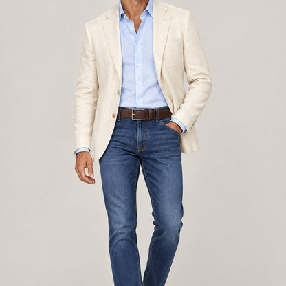 A man wearing blue jeans, a light blue button up shirt, a linen jacket and a dark brown pebbled leather belt with a satin silver buckle.