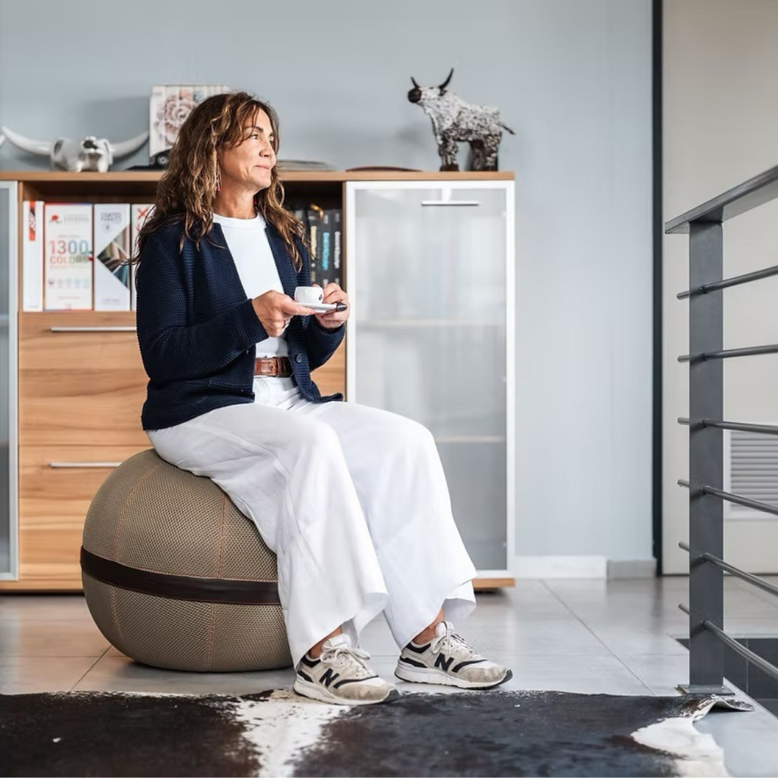 Woman sitting on a Balanball 65cm balance seat in a modern home office, holding an espresso cup