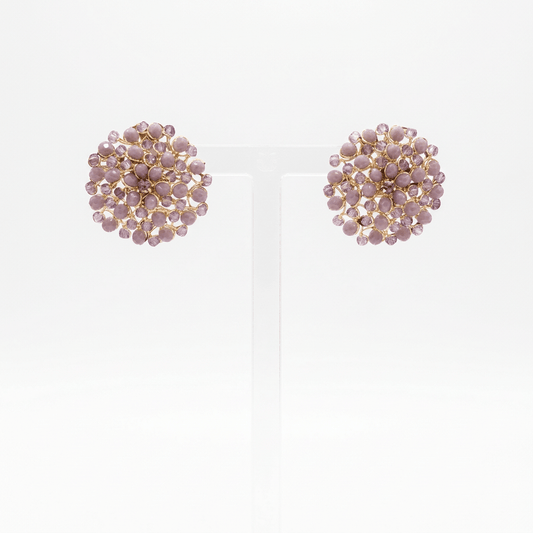 A lavender faceted button mandala earring on a perspex stand against a white background. 