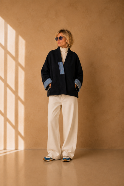 Nuno Milano Aki navy felted Merino wool jacket, front view, with contrasting light blue artisan patch detail and wide turned-back cuffs, open shawl collar, styled with cream wide-leg trousers