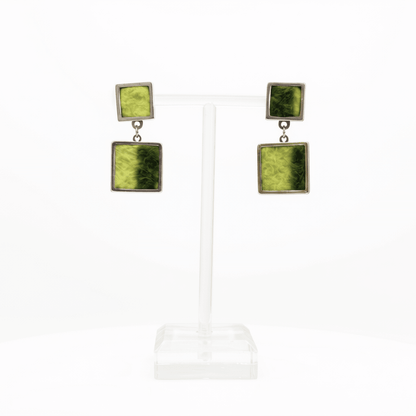 A pair of square drop earrings displayed on a clear acrylic T-stand against a white background. Each earring features a top silver-tone square with a lime & dark green marbled pattern, connected by a small silver chain to a larger bottom square of the same design.