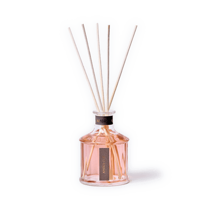 A reed diffuser bottle filled with pale pink liquid, featuring six natural reed sticks extending upward. The bottle is clear glass with a black collar and a vertical black label reading 'ARENO 00'.