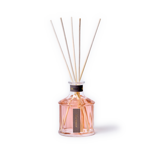 A reed diffuser bottle filled with pale pink liquid, featuring six natural reed sticks extending upward. The bottle is clear glass with a black collar and a vertical black label reading 'ARENO 00'.