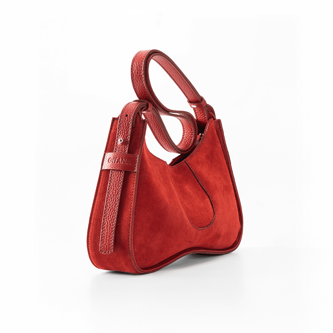 The Side View of Aria Shoulder Bag in Red Italian Suede Leather with Red Pebble Leather Trim.  Focus is on the Adjustable Shoulder Strap and the "Gitana" Brand