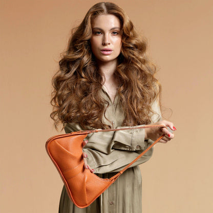 Woman holding an orange handbag against a beige background