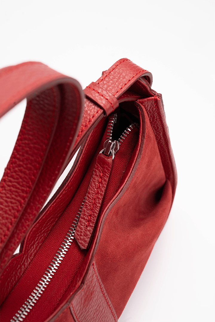 Close-up of a red suede leather handbag focusing on the zipper zipper detail.