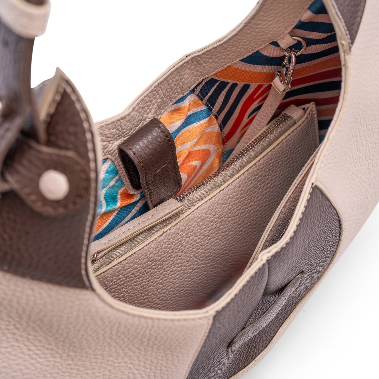 A close-up view of the inner colourful lining of a luxury cream and brown elliptical leather tote bag showcased  on a white background.  There is a matching pouch attached by a removable strap.
