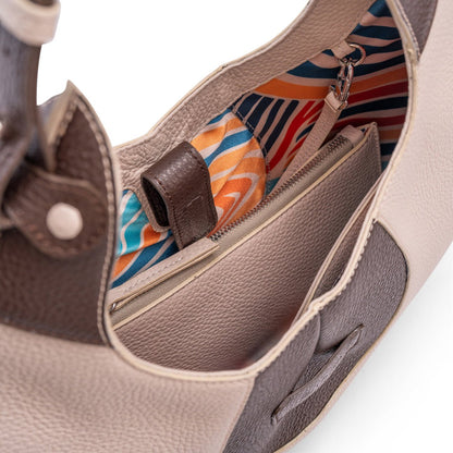 A close-up view of the inner colourful lining of a luxury cream and brown elliptical leather tote bag showcased  on a white background.  There is a matching pouch attached by a removable strap.