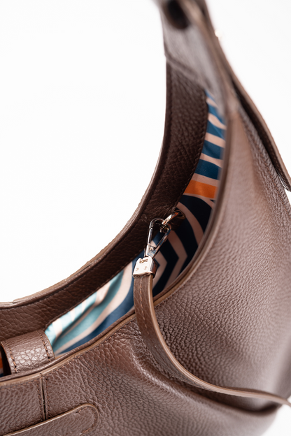 A close-up view of a brown Italian pebble caf leather tote bag with a striped lining on a white background