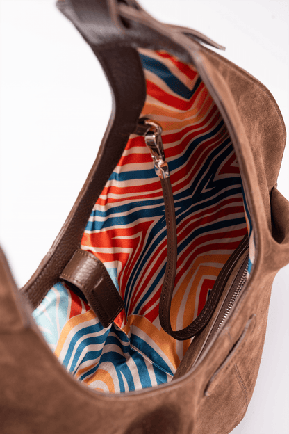 Top view of the Gitana suede shoulder bag in warm brown leather, showcasing the spacious interior with vibrant geometric striped lining, zip closure, and detachable inner leather pouch strap detail.
