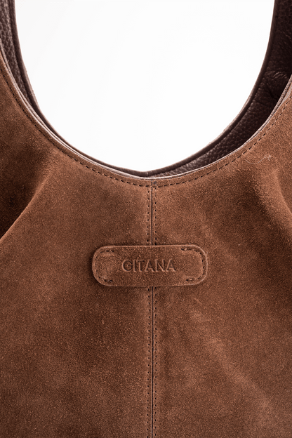 Close-up detail of the Gitana suede shoulder bag in warm  brown leather, featuring the embossed Gitana logo, curved top handle, contrast stitching, and soft textured suede finish.