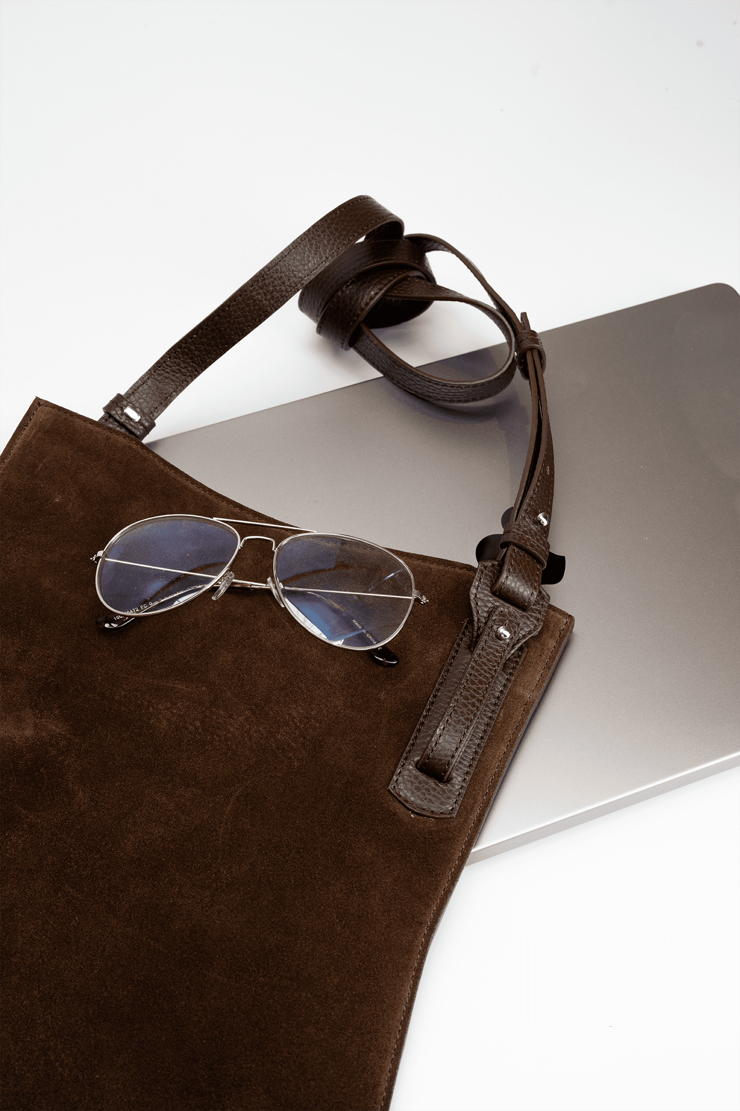 Brown suede leather crossbody handbag with sunglasses on a white background