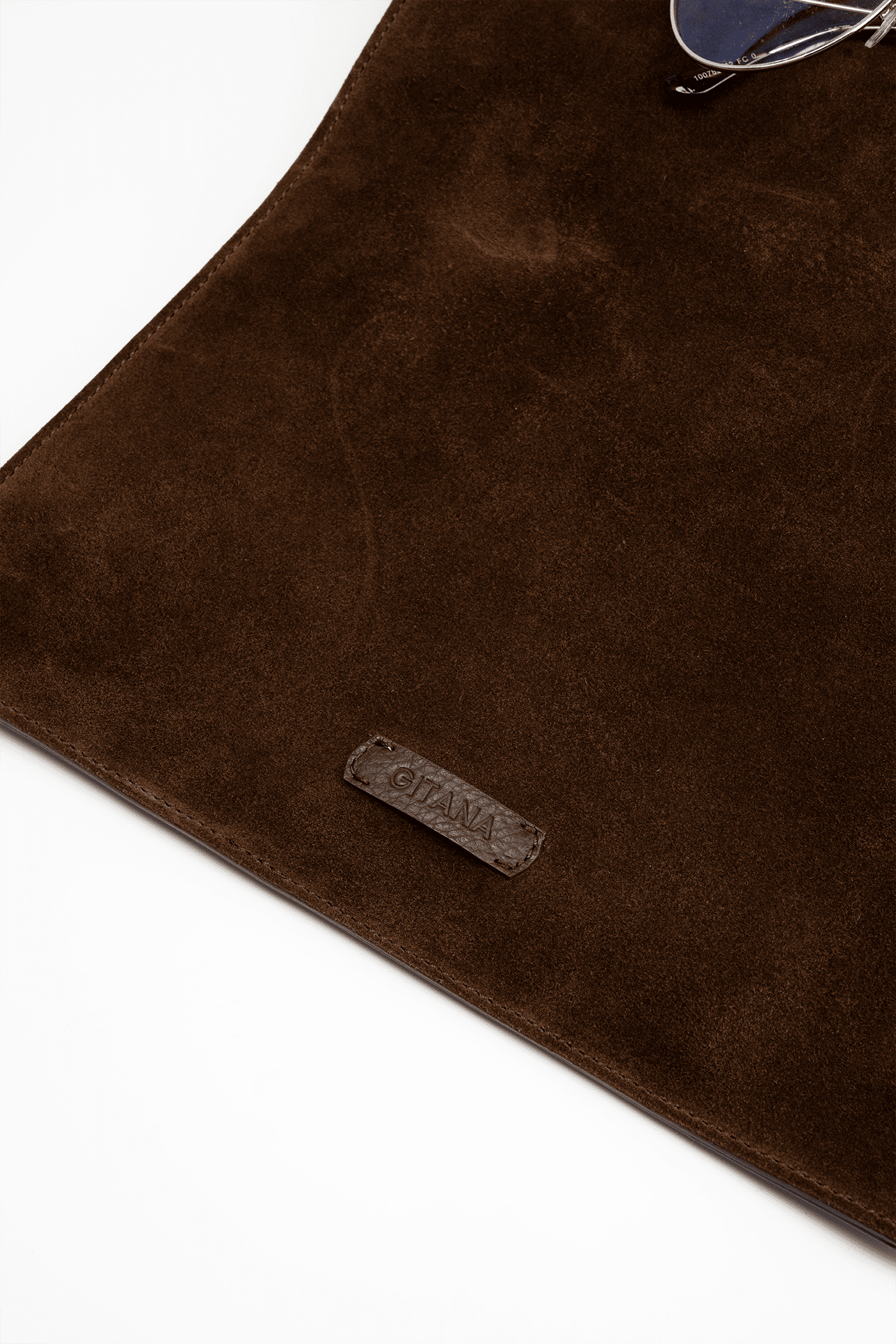 Brown suede leather handbag surface with the Gitana brand label on a white background