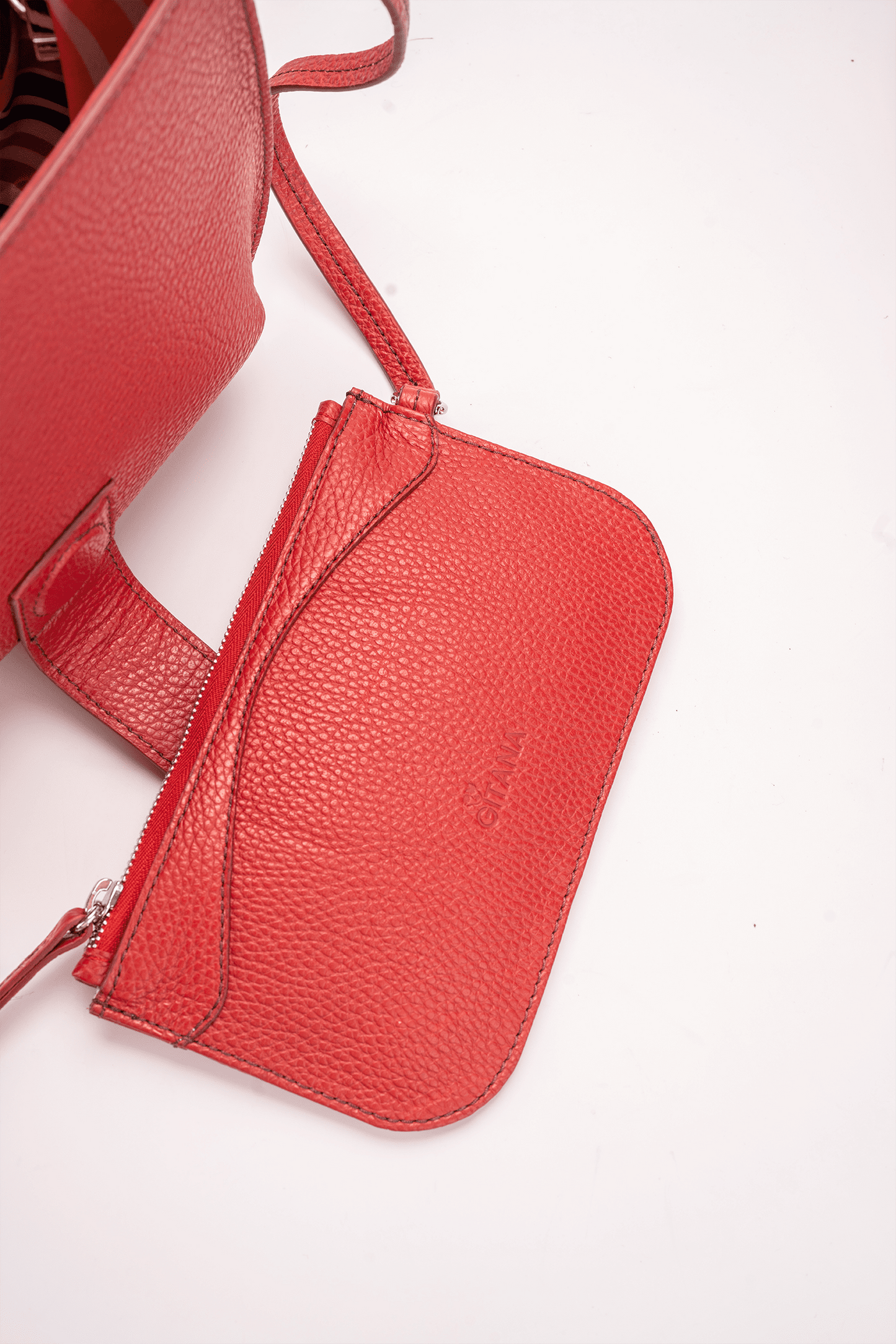 Close-up of a red Italian pebble calf leather designer pouch attached to a luxury handbag by a strap, showcasing the visible brand name.