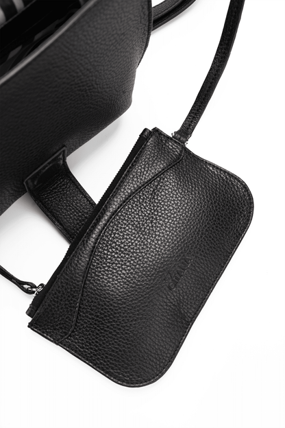 Close-up of a black leather designer pouch attached to a luxury handbag by a strap, showcasing the visible brand name.