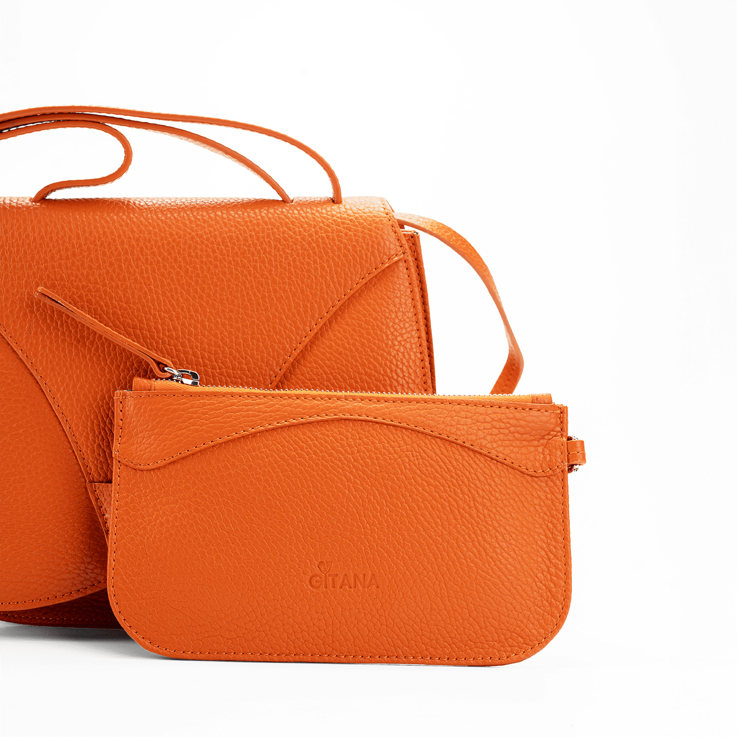 Close-up of an orange leather designer pouch attached to a luxury handbag by a strap, showcasing the visible brand name 