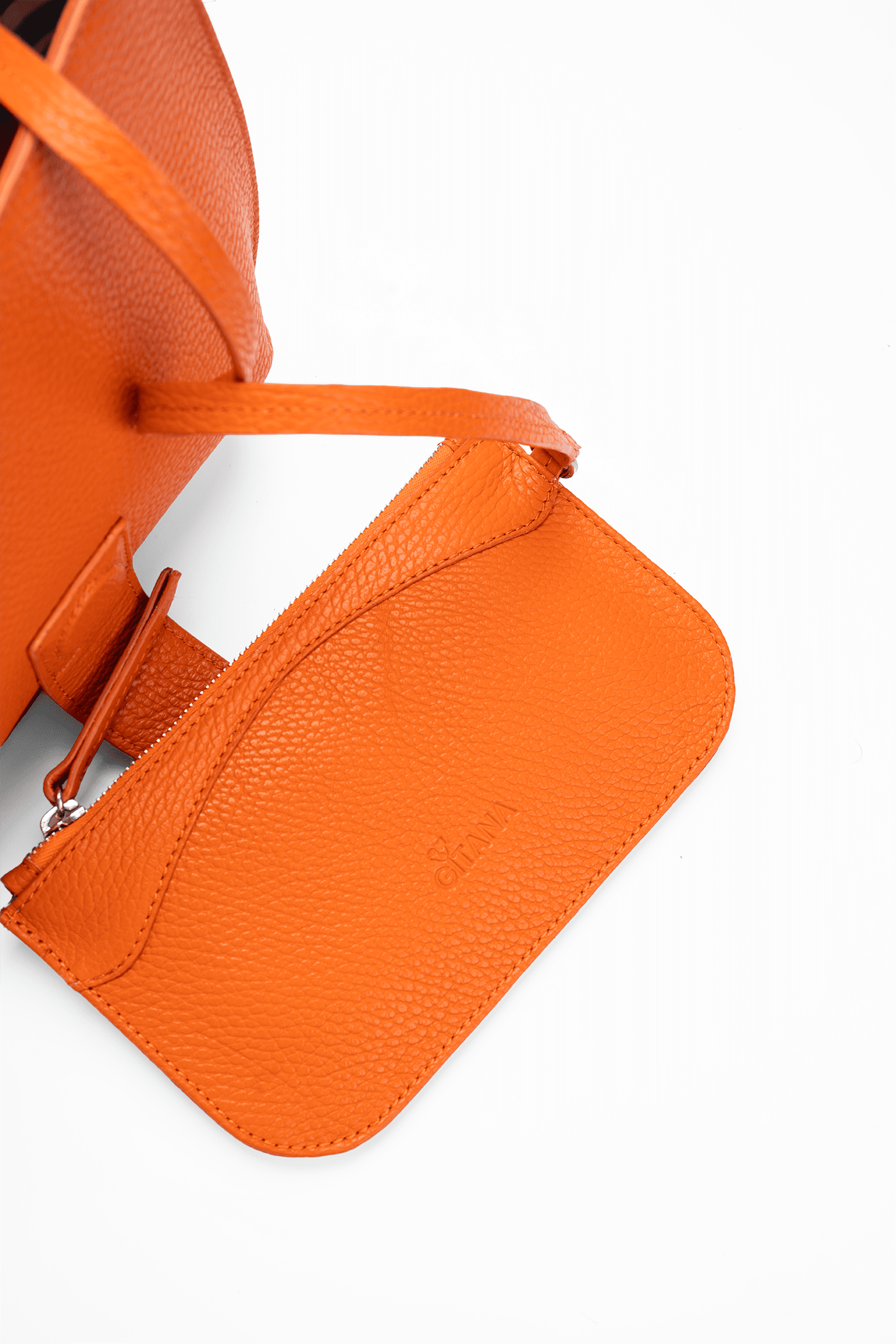 Close-up of an orange leather designer pouch attached to a luxury handbag by a strap, showcasing the visible brand name.
