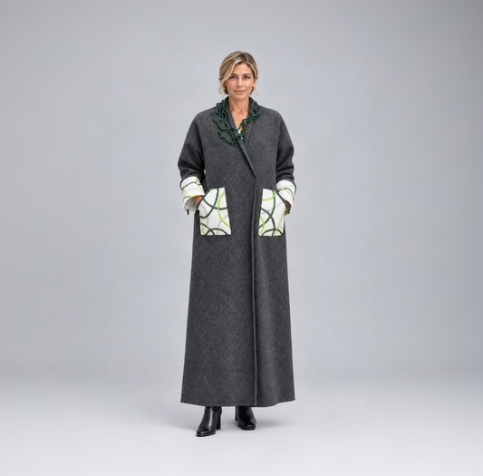 Une femme portant un long manteau gris anthracite en laine mélangée avec de grandes poches plaquées au motif abstrait blanc, vert et noir, avec un gros collier vert.