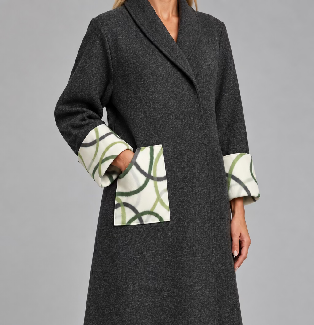 A woman wearing a grey Kimono gown coat made rom Nuno Felt  with detailed geometric design pockets and cuffs,  The design has olive green, chartreuse and grey geometrix lines on a white background.  The coat is made from 90% merino wool with 10% silk.
