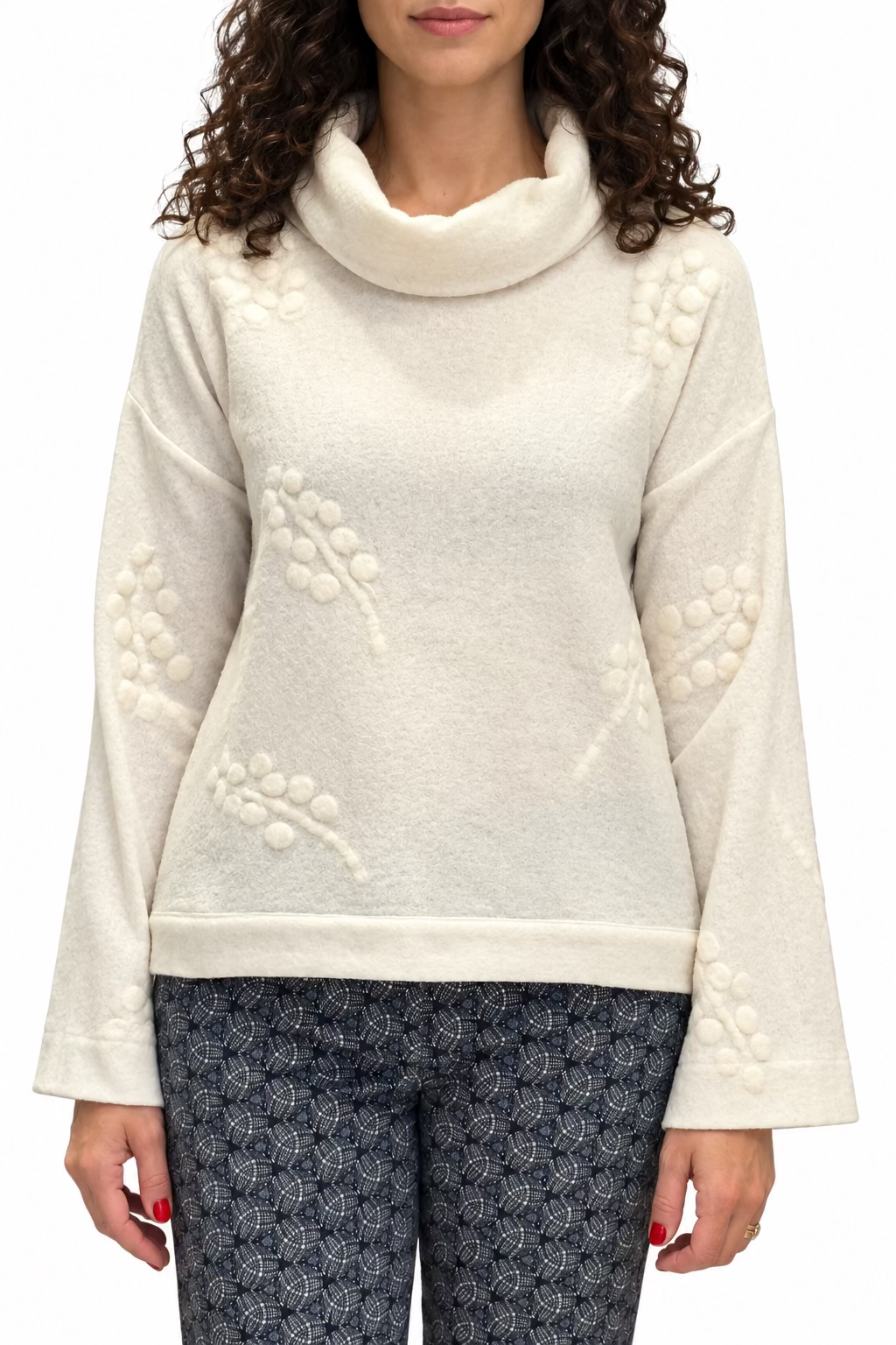 A woman wearing a cream merino wool cowl neck top with a cream grape design and patterned blue pants.