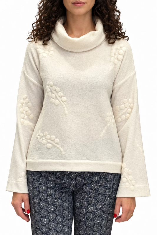 A woman wearing a cream merino wool cowl neck top with a cream grape design and patterned blue pants.