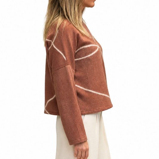 A woman shown from the side wearing a dusty rose cropped sweatshirt with white abstract curved line patterns, paired with cream tailored pants.
