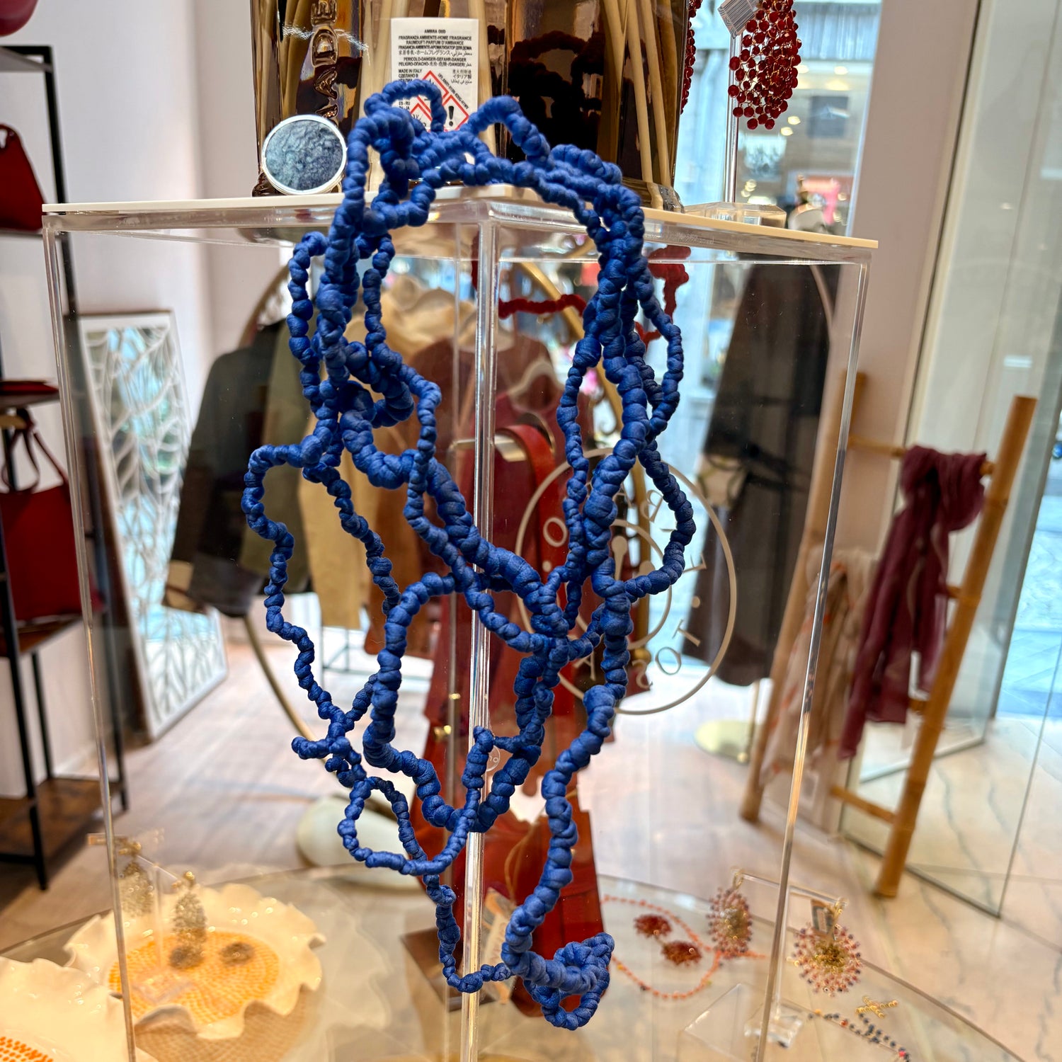 A bright blue knotted cord or rope accessory displayed inside a clear acrylic display case in a retail store setting.