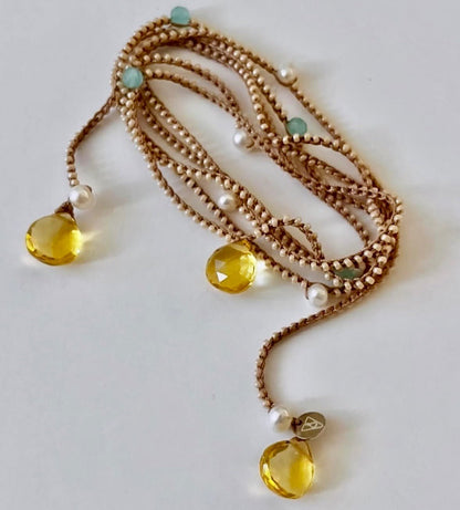 A multi-strand beaded necklace with gold-toned chains, white pearl beads, light blue round beads, and three faceted yellow crystal pendants, displayed on a light gray background.
