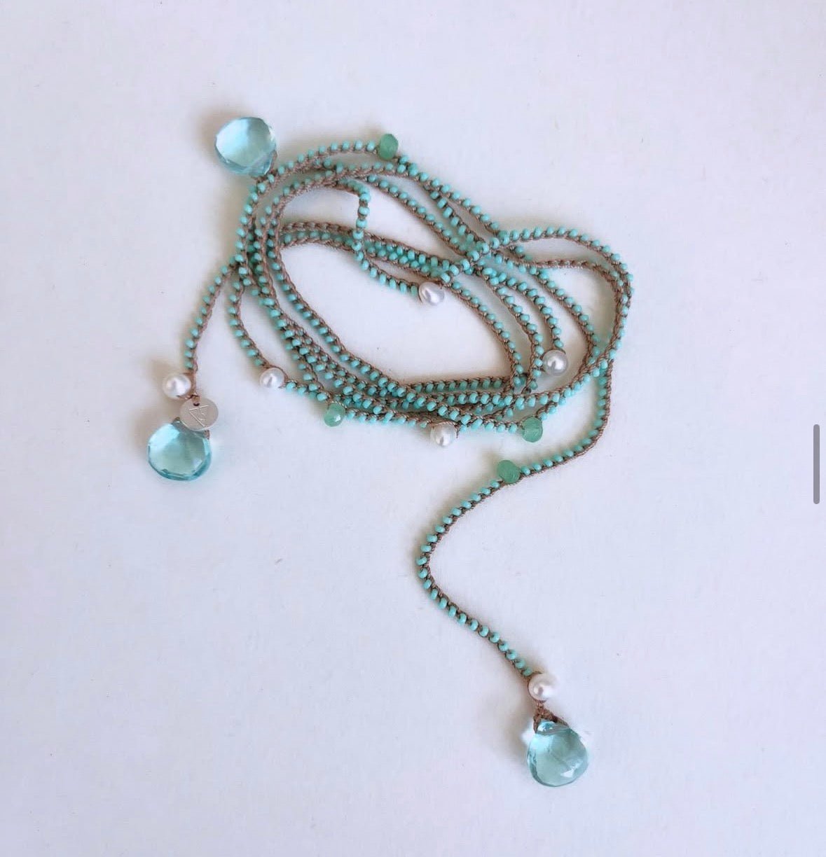 A long beaded necklace with mint green beads, small white pearl-like beads, and two light blue faceted crystal pendants on a plain white background.
