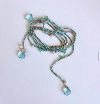 A long beaded necklace with mint green beads, small white pearl-like beads, and two light blue faceted crystal pendants on a plain white background.