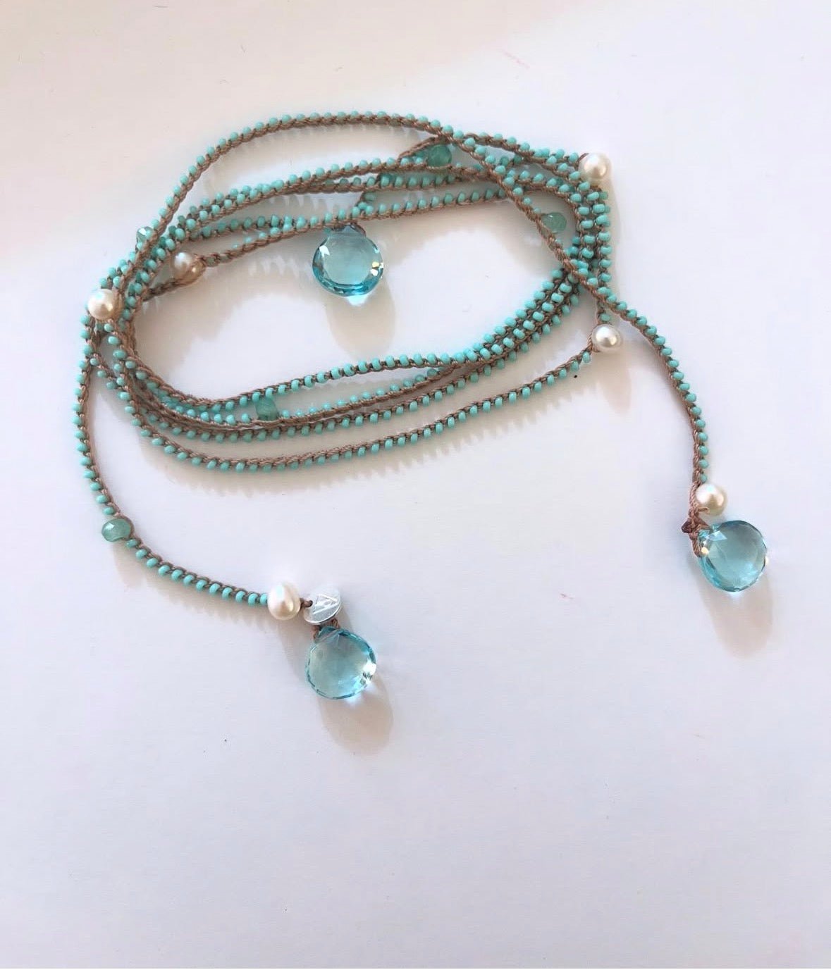 A multi-strand beaded necklace featuring turquoise beads, brown cords, white pearl-like accents, and two faceted light blue glass drop pendants, displayed on a plain white surface.