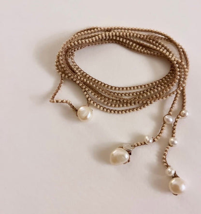 A multi-strand beaded necklace with white pearl-like drops, coiled on a plain light background.