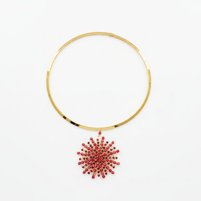 Gold-plated stainless steel rigid choker necklace with a handwoven 18kt gold-plated copper wire Mandàla pendant featuring ruby and garnet crystal beads, displayed on white marble.
