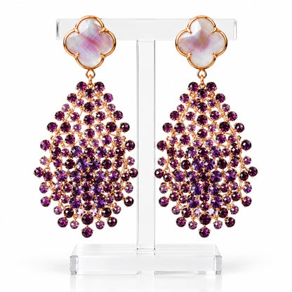 Boucles d'oreilles Mandàla tissées main en fil de cuivre plaqué or 18 ct avec cristaux de Bohême violets facettés et haut en cristal en forme de trèfle, sur un présentoir à bijoux.
