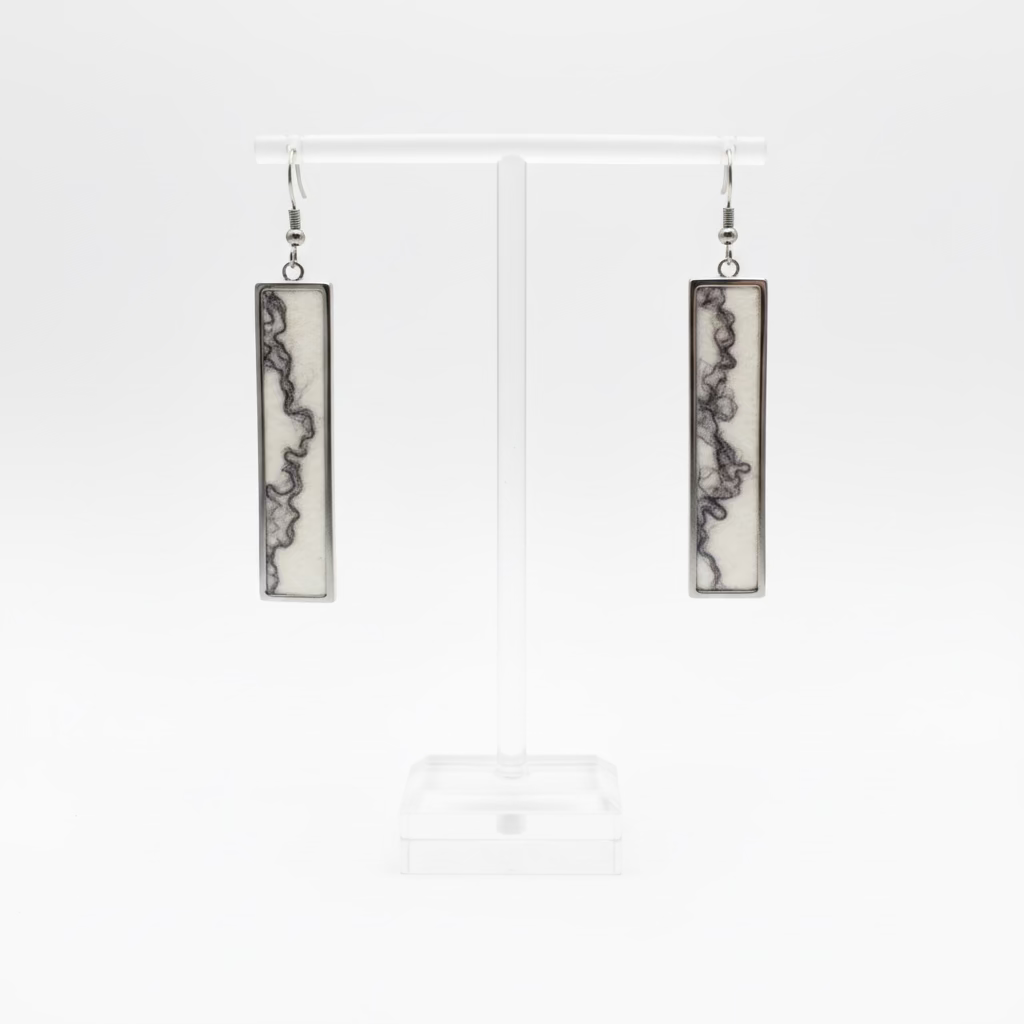 A pair of rectangular long pendant earrings with dark abstract marbled patterns on a cream background, displayed on a clear acrylic stand with a white background.