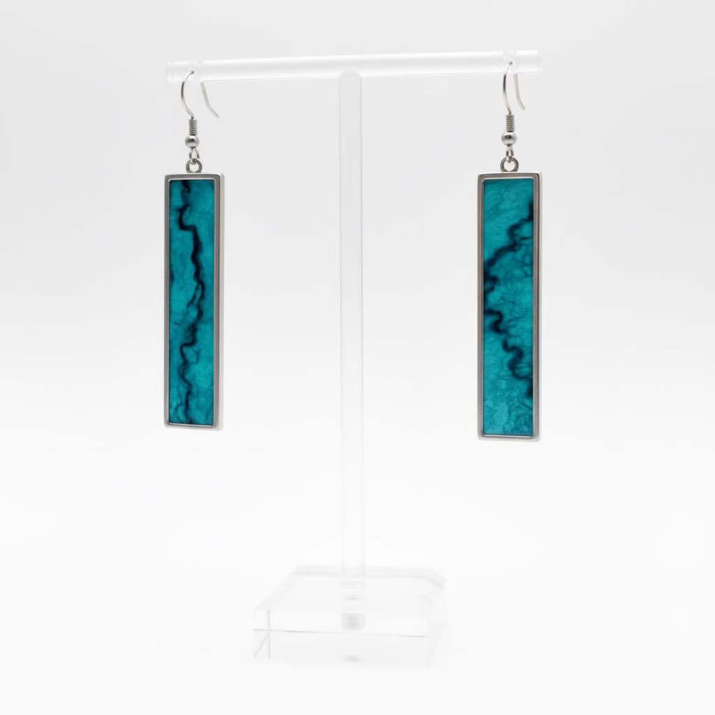 A pair of rectangular drop earrings with turquoise blue and black marbled inlay and silver-toned metal borders, displayed on a clear acrylic stand against a white textured wall.