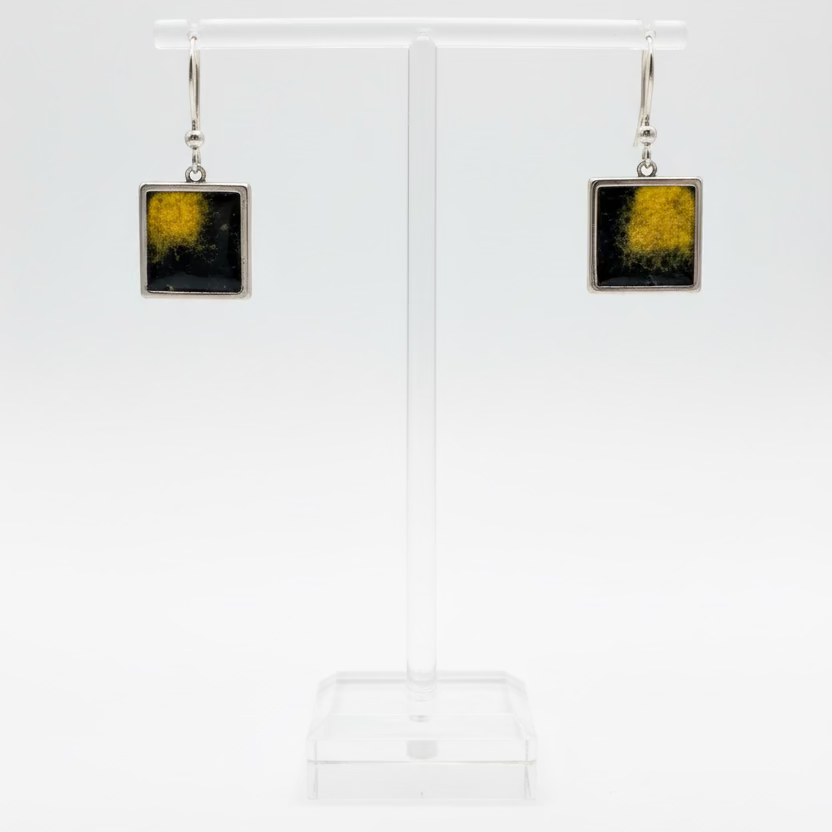 A pair of square drop earrings with a textured yellow and black Nuno Felt center and silver-tone borders, displayed on a clear acrylic stand against a white background.