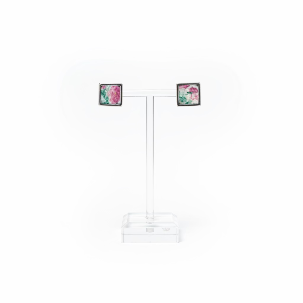 A pair of square stud earrings with colorful floral inlay and gold-toned and silver-toned borders, displayed on a clear acrylic T-stand with a white background.